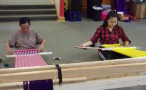 A KOM youth and adult weaver weave next to each other during the summer weaving class
